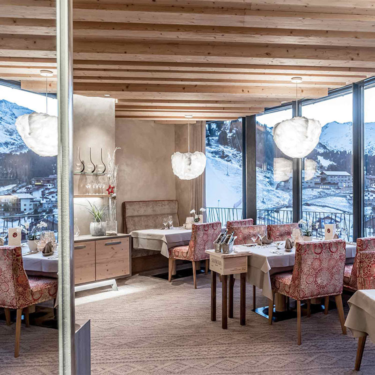 Das Bild zeigt den Gastronomiebereich des Hotel Haid & Falkner Gotthard Zeit ****S am Obergurgl. Auf der rechten Seite sind Panoramafenster zu sehen, die einen Blick auf eine Schneelandschaft bieten.