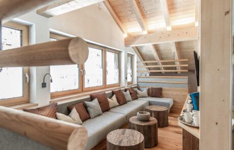 Auf dem Bild ist der Aufenthaltsbereich im Hotel "Im Franzerl" am Weissensee in Kärnten zu sehen. In der Mitte des Raumes steht eine moderne graue Couch, die zum Entspannen einlädt. Über dem Aufenthaltsbereich erstrecken sich Dachbalken aus hellem Holz, die eine warme und gemütliche Atmosphäre schaffen.